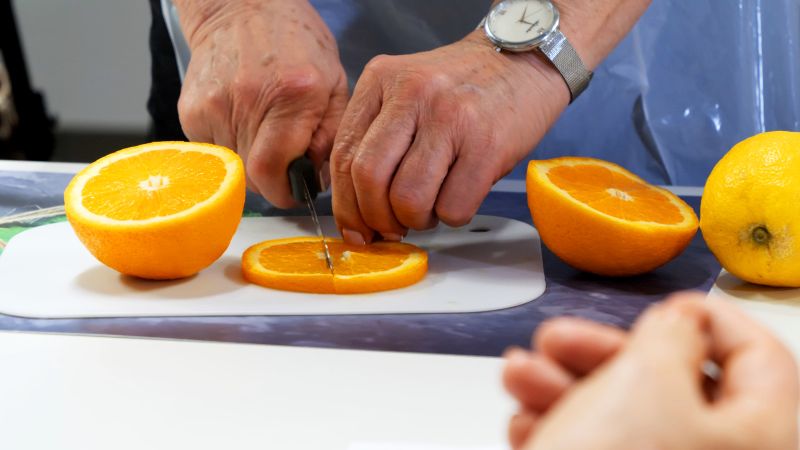 Fotografia - zbliżenie na dłonie kucharza krojącego pomarańczę.