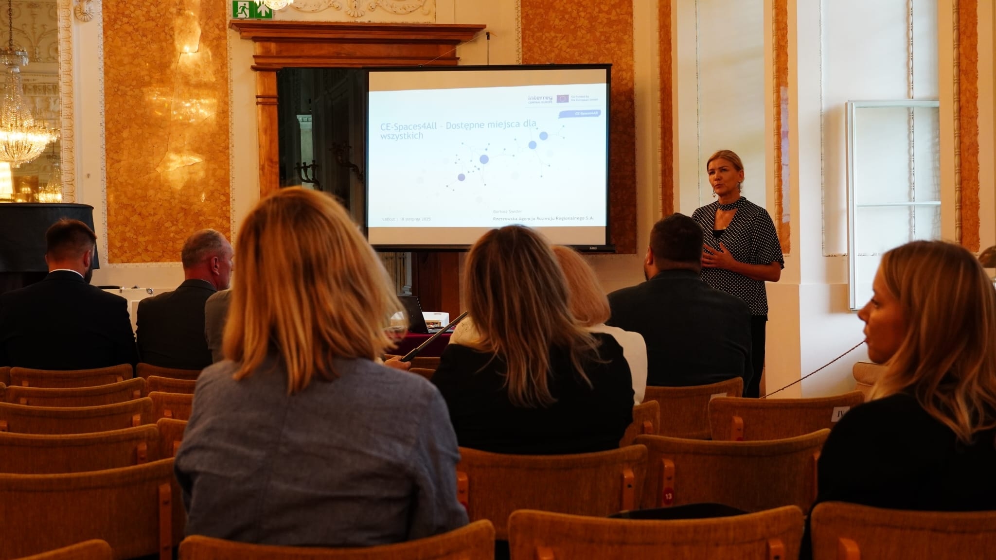 Sala Balowa, Dyrektor Ośrodka Garncarskiego w Medyni Głogowskiej mówi do zebranych, stoi. Przed nią siedzący słuchacze.  W tle prezentacja multimedialna na ekranie.