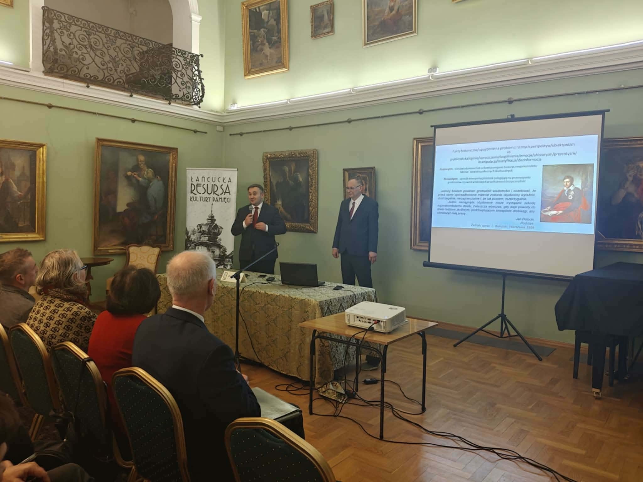 XIX Łańcucka Resursa Kultury Pamięci - przemawiają dr Piotr Szopa, dyrektor MZŁ i dr Andrzej Borcz, w tle prezentacja z treściami wykładu oraz baner ŁRKP