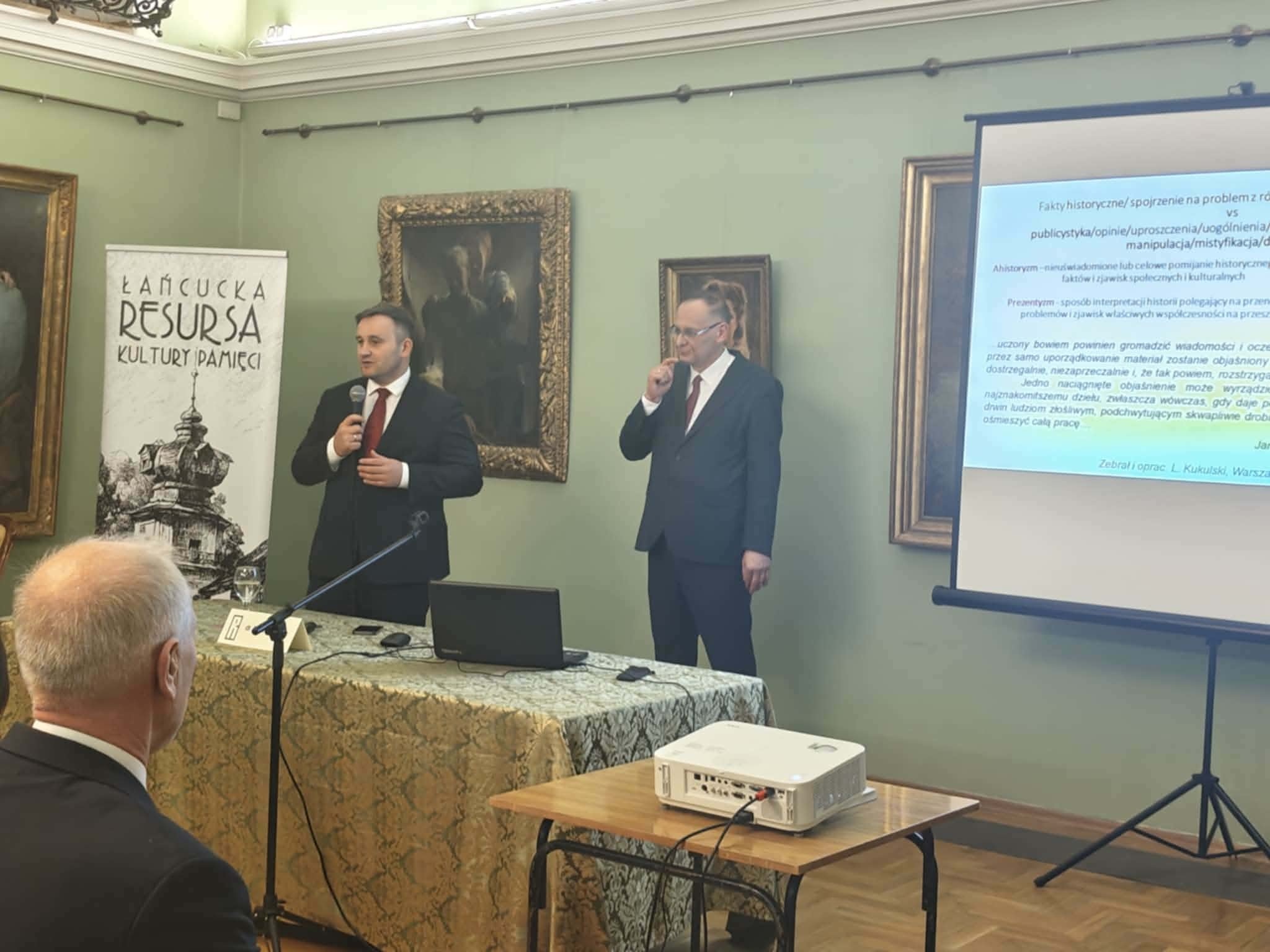 XIX Łańcucka Resursa Kultury Pamięci - przemawiają dr Piotr Szopa, dyrektor MZŁ i dr Andrzej Borcz, w tle prezentacja z treściami wykładu oraz baner ŁRKP