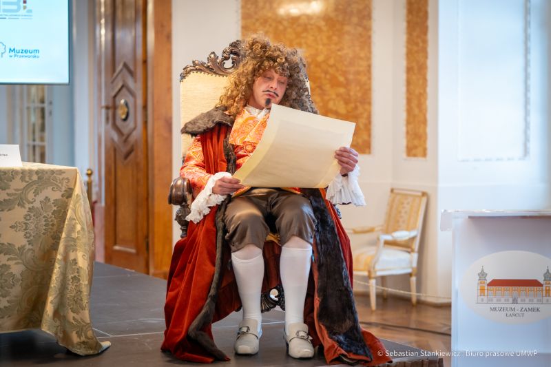Sala Balowa, aktor w stroju z epoki sarmackiej z odczytem, siedzi