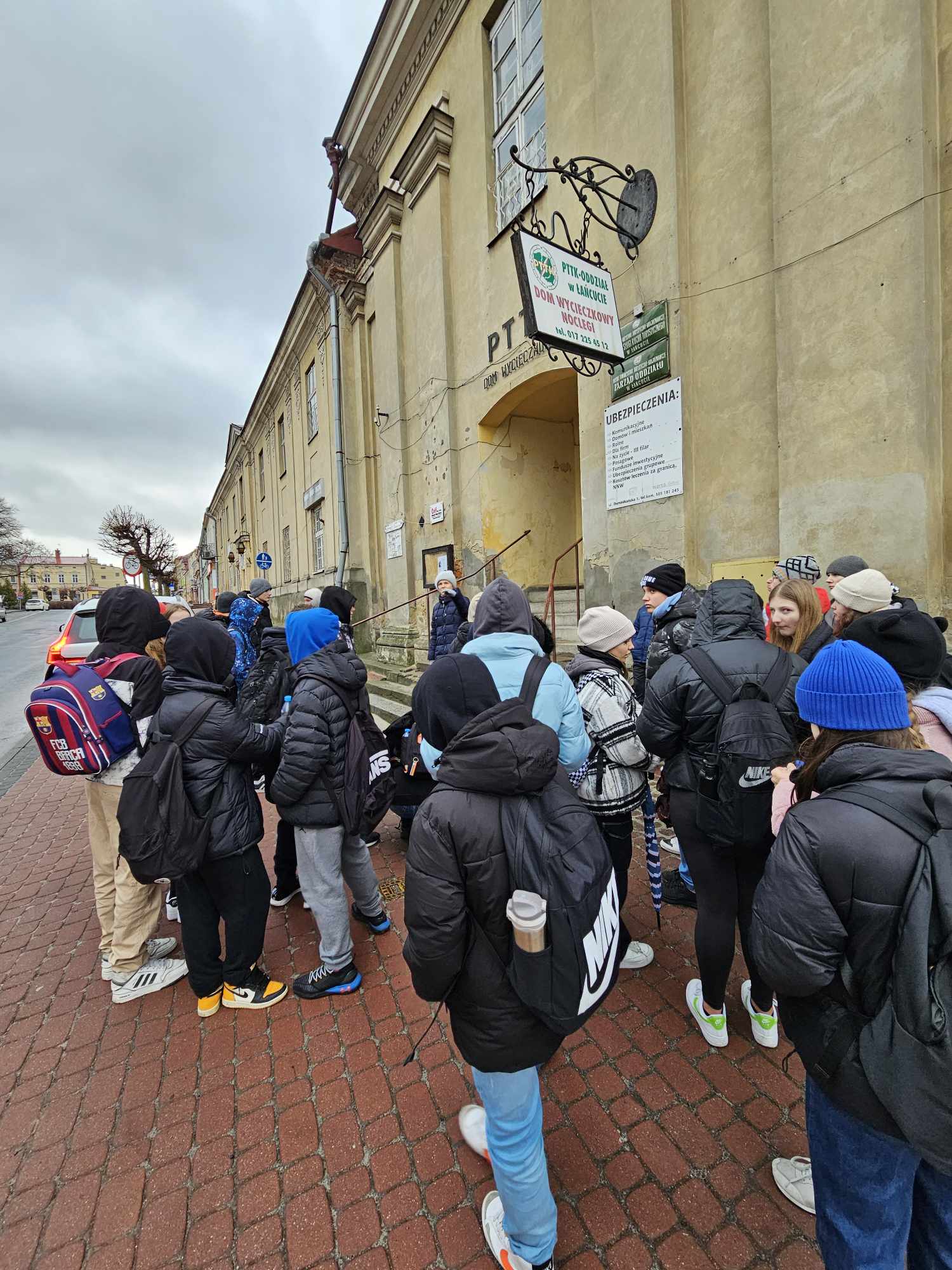 Wykład kierownik Joanny Kluz. Obok budynku PTTK w Łańcucie z grupą uczniów.