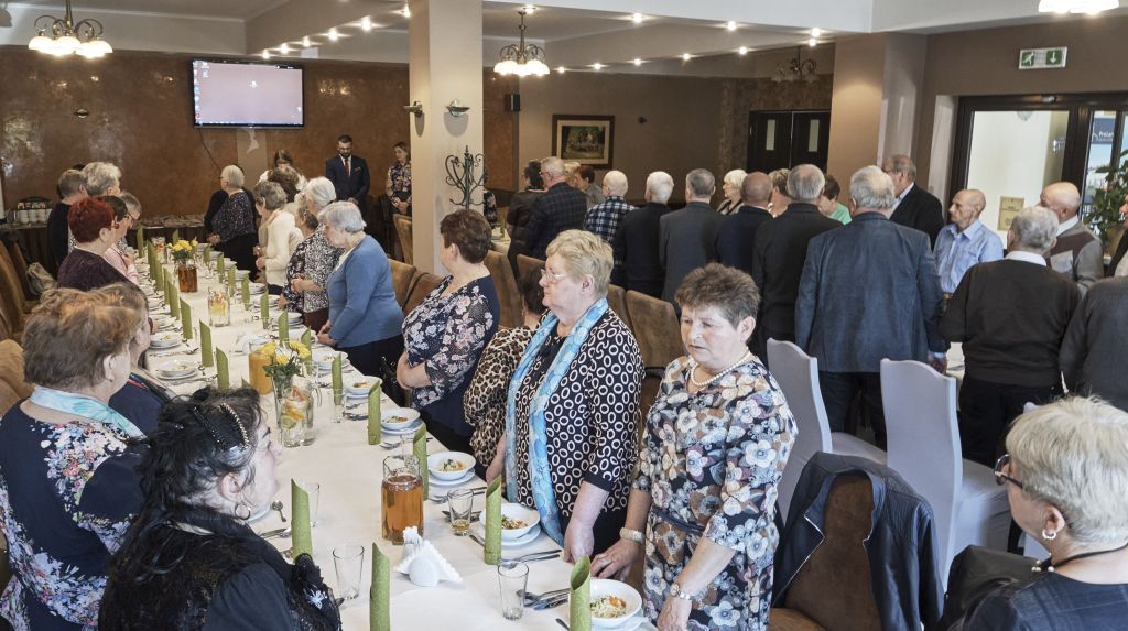 Goście wydarzenia stoją wokół stołu bankietowego. Na środku sali przemawiają p. o. Dyrektora Muzeum - Zamek w Łańcucie Krzysztof Żaba, Główna Księgowa Marzena Machniak, Przewodnicząca Związków Zawodowych "Solidarność" Muzeum - Zamek w Łańcucie Bożena Lauzer.