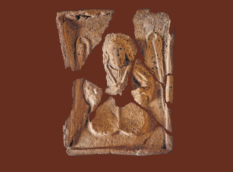 Fragment okładki książki "Dawne wzgórze zamkowe w Łańcucie.  Wyniki badań archeologicznych z 2017 r.". Bordowe tło. Na pierwszym planie zdjęcie połamanego i ułożonego kafla (wykopalisko archeologiczne). Kafel przedstawia anioła.