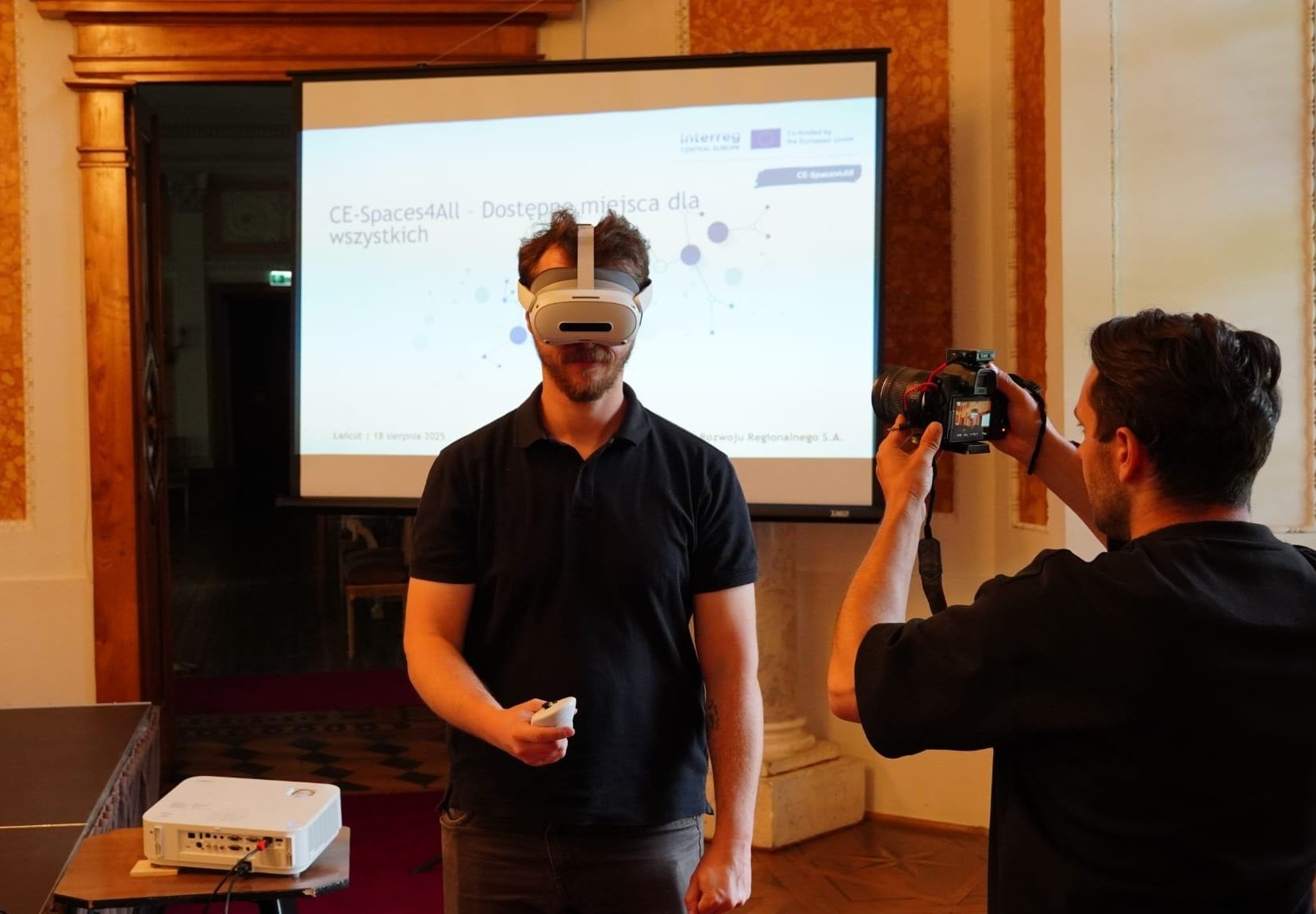 Sala Balowa, mężczyzna stoi, ma założone gogle VR, inny mężczyzna wykonuje mu zdjęcie